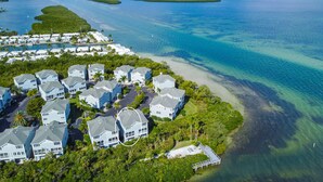 An aerial view of a coastal residential area with houses, a beach, and clear blue waters. - Tranquil Bay Views – Cedars East #812 by RVA (Longboat Key)