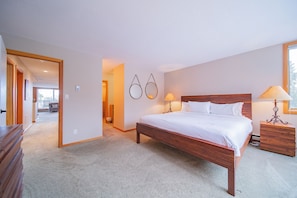 Une chambre à coucher avec un lit en bois, deux tables de chevet avec des lampes, un sol recouvert de moquette et un couloir menant à une autre pièce.