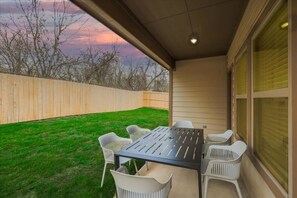 Relax on the patio surrounded by a lush yard and trees, with a table and chairs for a peaceful outdoor space.
