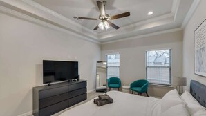 A bedroom with a bed, a TV, a dresser, two chairs, and a ceiling fan. - Your Vibrant Dallas Getaway Home (Dallas)
