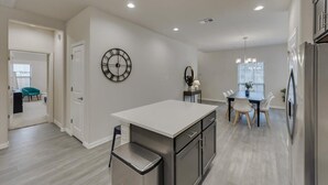 A modern kitchen with a central island, a dining area with a chandelier, and a large wall clock. - Your Vibrant Dallas Getaway Home (Dallas)