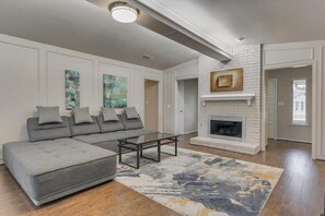 A living room with a sectional sofa, a fireplace, and abstract wall art. - Spacious and Modern Home with Private Pool (Plano)