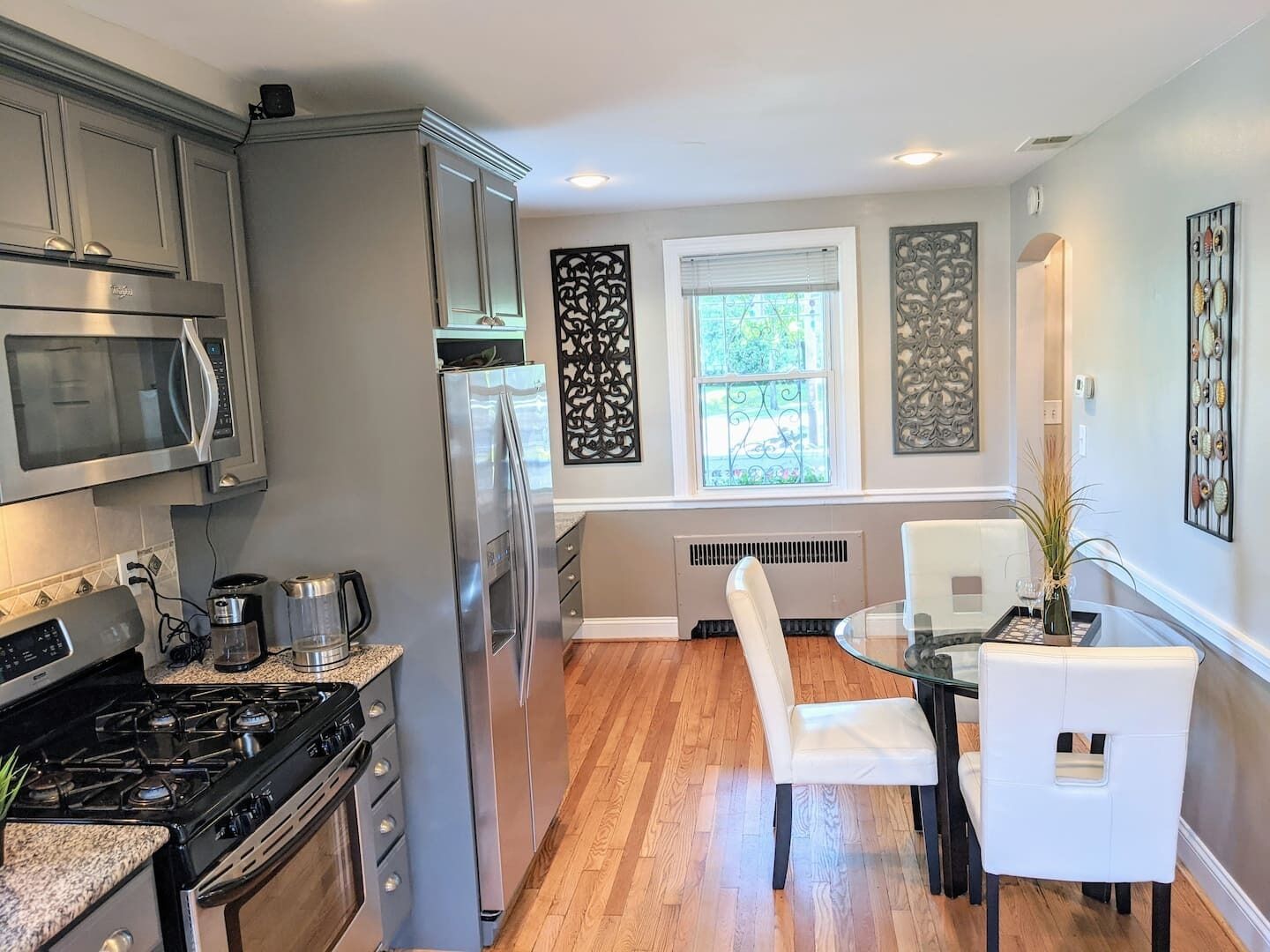 Una cocina moderna con electrodomésticos de acero inoxidable, un comedor con mesa de vidrio y sillas blancas, y decoración mural.