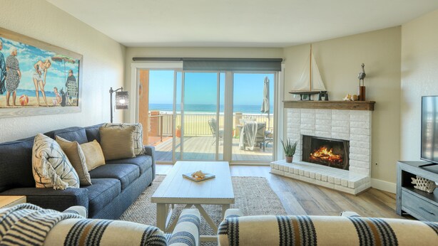 A living room with a sofa, coffee table, fireplace, and a view of the ocean through large sliding glass doors.