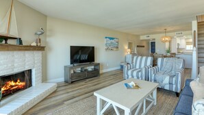 A living room with a fireplace, a television, striped furniture, and a beach-themed painting.