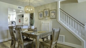 A dining area with a glass table, wooden chairs, and a hanging light fixture.