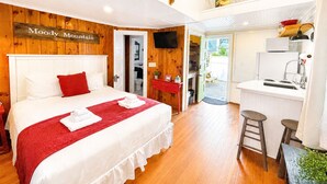 Habitación de hotel con cama, escritorio, kitchenette y baño visible a través de una puerta abierta.