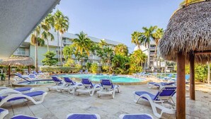 A poolside area with lounge chairs and a pool, surrounded by palm trees and a building with balconies. - Island Time | Luxury Beach Condo w/ Pool & Hot Tub (Key West)