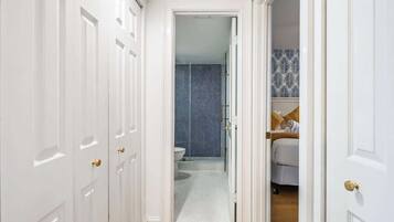 A hallway with white doors leading to a bathroom with a patterned shower wall and a bed with a patterned bedspread.