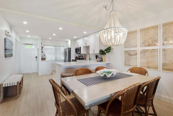 Cozinha moderna com armários brancos, uma ilha central e um espaço de jantar com cadeiras de vime e um lustre.