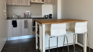 A modern kitchen with wooden cabinets, a built-in stove, and a bar area with white chairs. - Apt With Panoramic View Near Vauban City (Briançon)