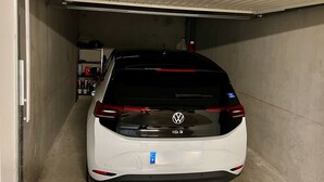 A white Volkswagen ID.3 parked in a narrow garage with a concrete floor and metal garage door. - Apt With Panoramic View Near Vauban City (Briançon)