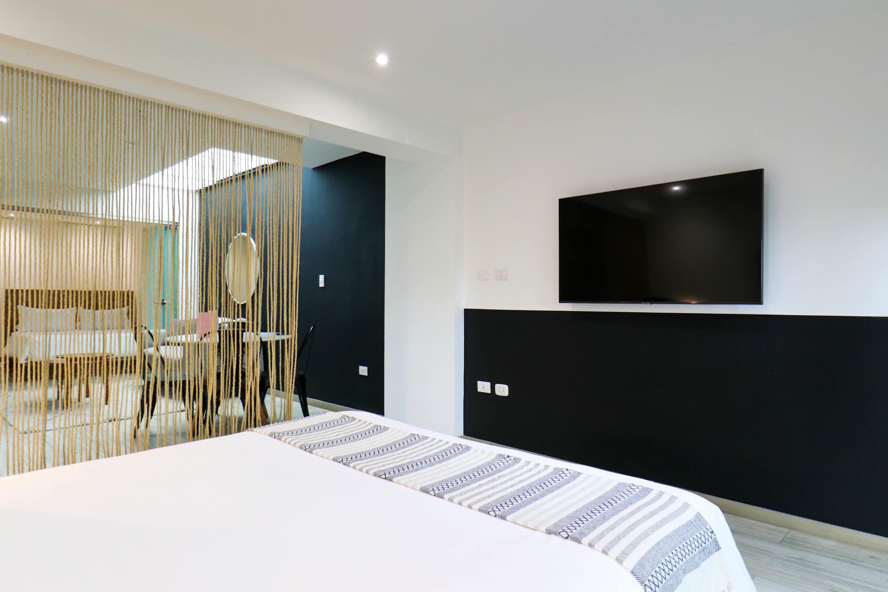 Una camera da letto moderna con un letto grande, una TV a parete e un paravento con linee verticali.