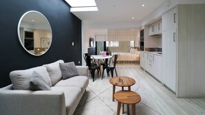 A modern living space with a sofa, a round mirror, a dining table with chairs, and a kitchen area.