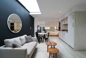 A modern living space with a sofa, a round mirror, a dining table with chairs, and a kitchen area.