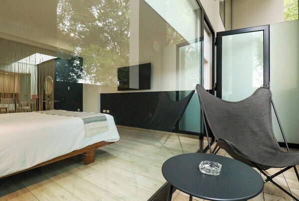 A modern hotel room with a bed, a small table, a chair, and a large window.