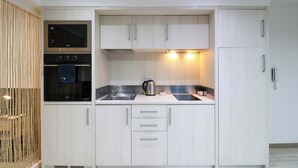 A compact kitchen with a built-in oven, a kettle, and a sink.