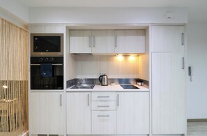 A compact kitchen with a built-in oven, a kettle, and a sink.