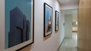 Un couloir avec des tableaux encadrés accrochés au mur, un plancher en bois et une porte au fond.