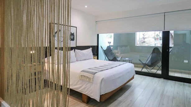 Une chambre moderne avec un grand lit, une porte vitrée donnant sur un balcon et un rideau décoratif.