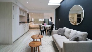 Un salon moderne comprenant un canapé, deux petites tables en bois, un miroir rond et un coin repas avec une table et des chaises.