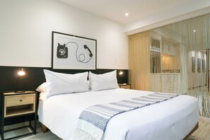 A hotel room with a large bed, two bedside tables, a framed picture on the wall, and a window with curtains.