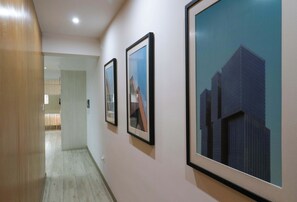 A corridor with framed pictures on the wall, leading to a room with a window.
