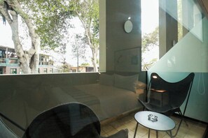 A balcony with a view of trees and buildings, a small table with a chair, and a wall-mounted light fixture.