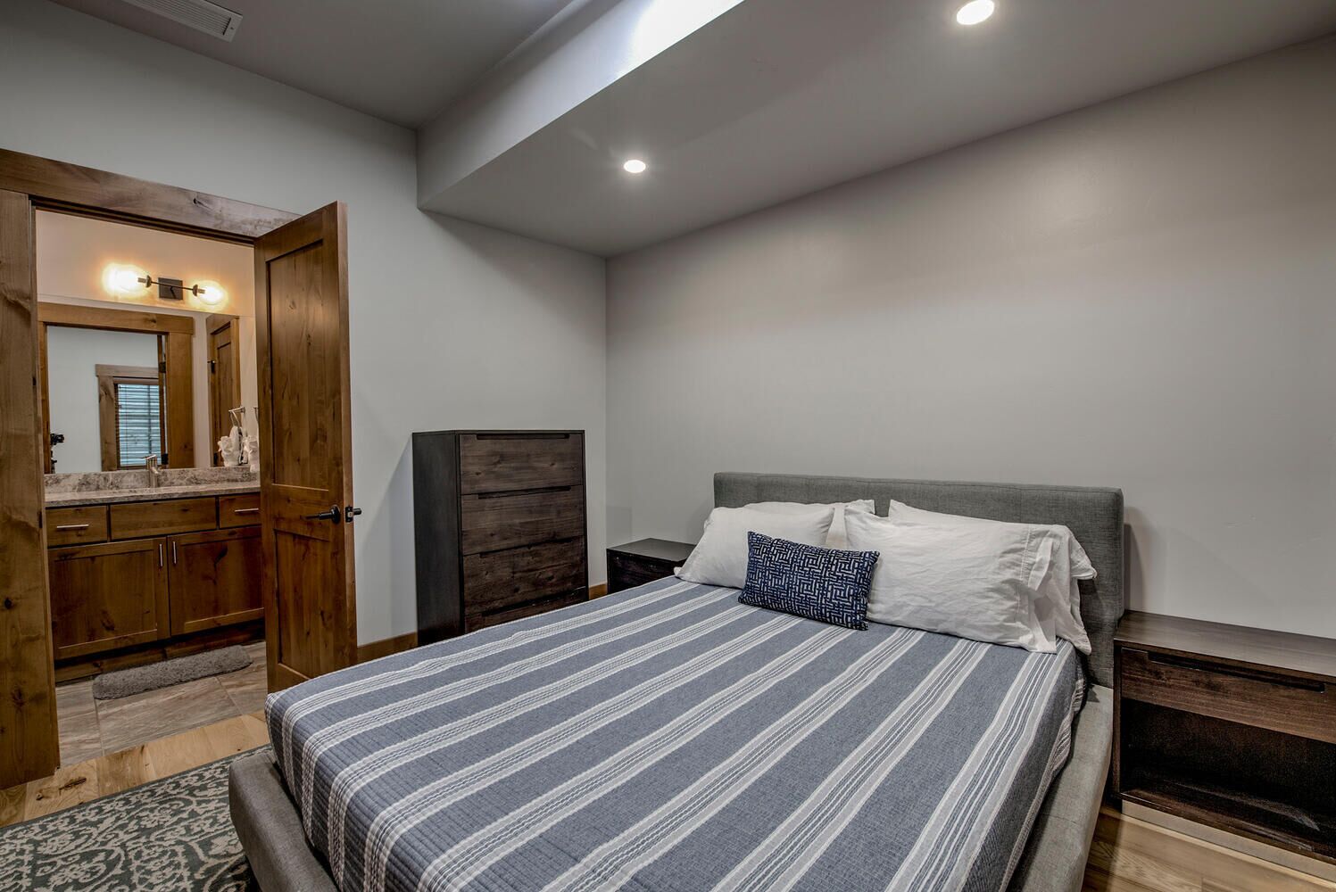 Een slaapkamer met een bed, nachtkastje, dressoir en spiegel.