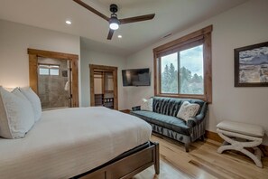 A bedroom with a large bed, a sofa, a TV, and a window with a view of trees. - Mountain Lodge Oasis | 6BR w/ Hot Tub Near Aspen (Carbondale)