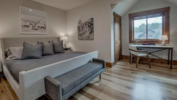 A bedroom with a large bed, a desk, and a chair. There are two wall-mounted lamps and a window with a view of trees. - Mountain Lodge Oasis | 6BR w/ Hot Tub Near Aspen (Carbondale)