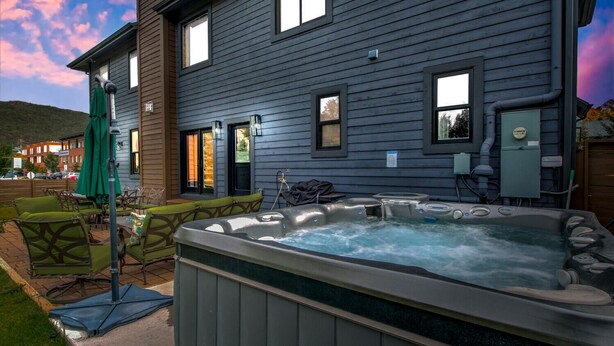 Un jacuzzi situé devant une maison, avec un patio, des sièges d’extérieur et une vue sur la rue.