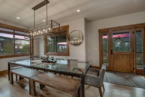 A modern dining area with a glass table, wooden benches, and a pendant light. - Mountain Lodge Oasis | 6BR w/ Hot Tub Near Aspen (Carbondale)