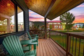 A wooden deck with green Adirondack chairs, a stone wall, and a view of a building complex and hills in the distance. - Mountain Lodge Oasis | 6BR w/ Hot Tub Near Aspen (Carbondale)