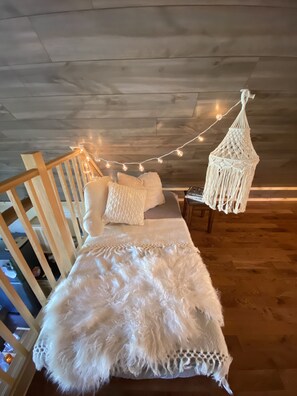 A cozy bedroom with a wooden ceiling, a bed with white bedding, and a macramé hanging light fixture.
