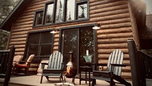 A log cabin with a porch, three Adirondack chairs, a fire pit, and large windows. - Peaceful river front cabin in the WOODS! Kayak, snowmobile, hike, relax! (Rhinelander)