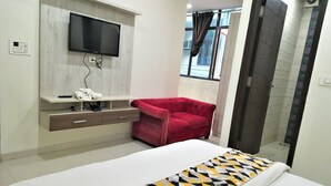 Une chambre à coucher avec un lit, un fauteuil rouge, un téléviseur fixé au mur et un espace douche.