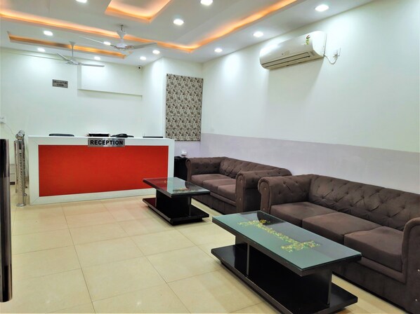 A reception area with a red counter, two brown sofas, a glass coffee table, and a ceiling fan.