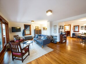 A spacious living room with a blue sofa, wooden chairs, a coffee table, and a fireplace.