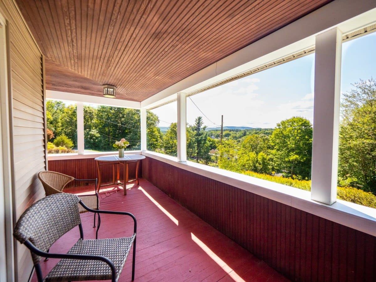 En inglasad veranda med ett bord och stolar, stora fönster som ger utsikt över grönområden och kullar.