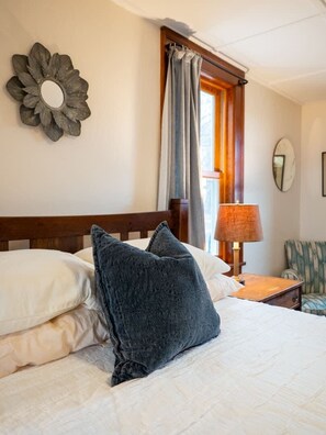 A neatly made bed with a dark blue pillow, a wooden headboard, a bedside lamp, and a flower-shaped wall decoration.