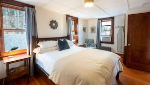 A bedroom with a large bed, wooden floor, a desk with a lamp, a chair, and a wardrobe. - Centrally Located Historical Home (Lee)