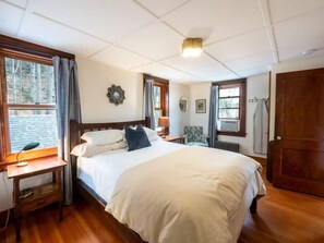 A bedroom with a large bed, wooden floor, a desk with a lamp, a chair, and a wardrobe. - Centrally Located Historical Home (Lee)