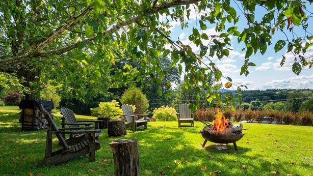 A grassy outdoor area with a fire pit, lounge chairs, and a wooden table. - Centrally Located Historical Home (Lee)