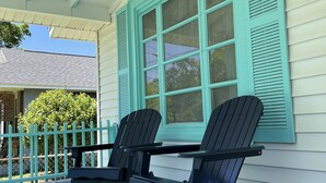 A porch with two Adirondack chairs, a table, and a teal window with shutters.