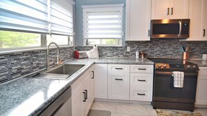 A modern kitchen with white cabinets, a stainless steel microwave, a black oven, and a tiled backsplash.