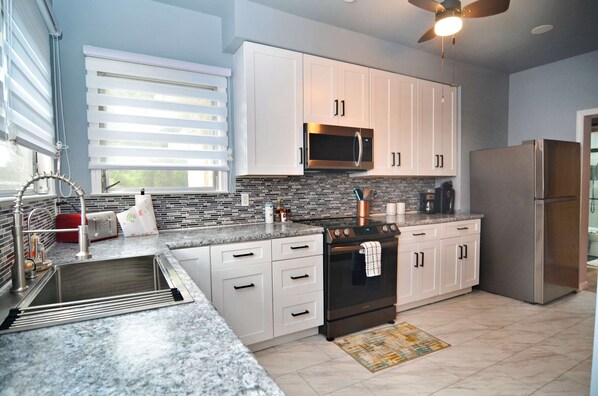 A modern kitchen with white cabinets, a stainless steel refrigerator, a microwave, and a built-in oven.