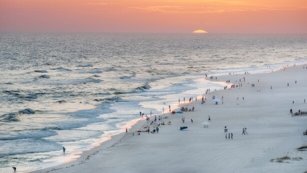 A beach with people walking and sunbathing.