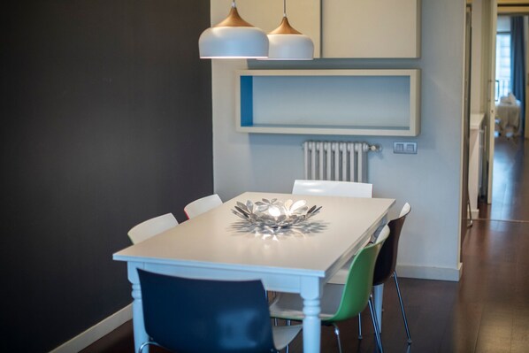 A modern dining area with a white table, green and white chairs, and pendant lights.