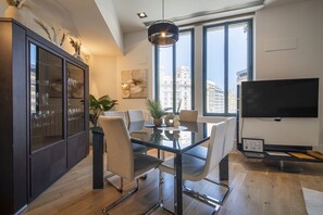 Uma sala de jantar moderna com mesa de vidro, cadeiras, televisão e vista para a cidade.